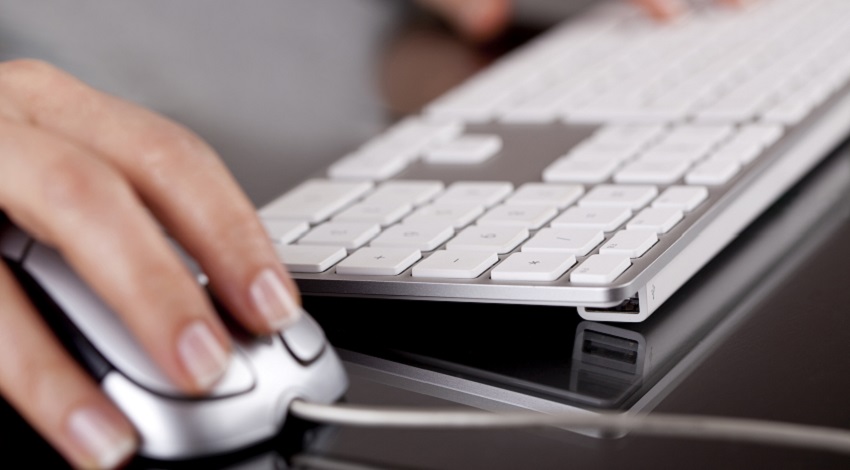 A hand on a computer mouse next to a keyboard