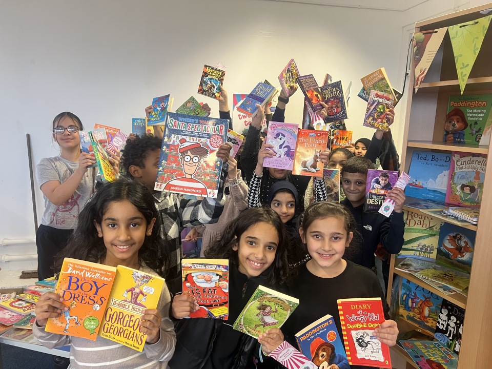 A group of smiling school children posing together while holding up a variety of popular children&rsquo;s books in a bright room.