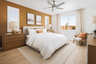 bedroom with wood floors, three windows, tan upholstered bed with white bedding, and large wood nightstands
