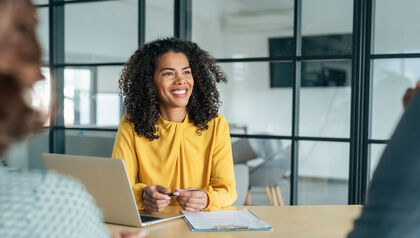 Business woman in a yellow blouse sitting at a conference table with laptop