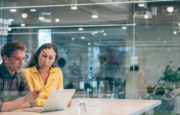 Man and woman at a desk looking at a laptop