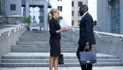 Professional woman and man talking outside in front of concrete stairs