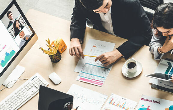Group of coworkers at a desk looking at documents and laptops