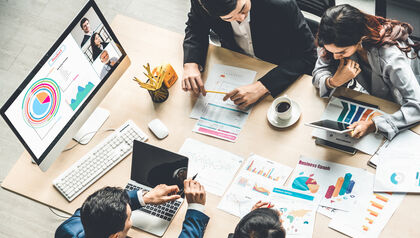Group of coworkers at a desk looking at documents and laptops