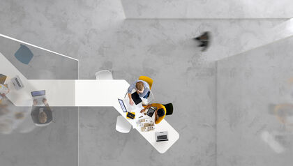 Top-down view of two co-workers sitting at a long table looking at laptops