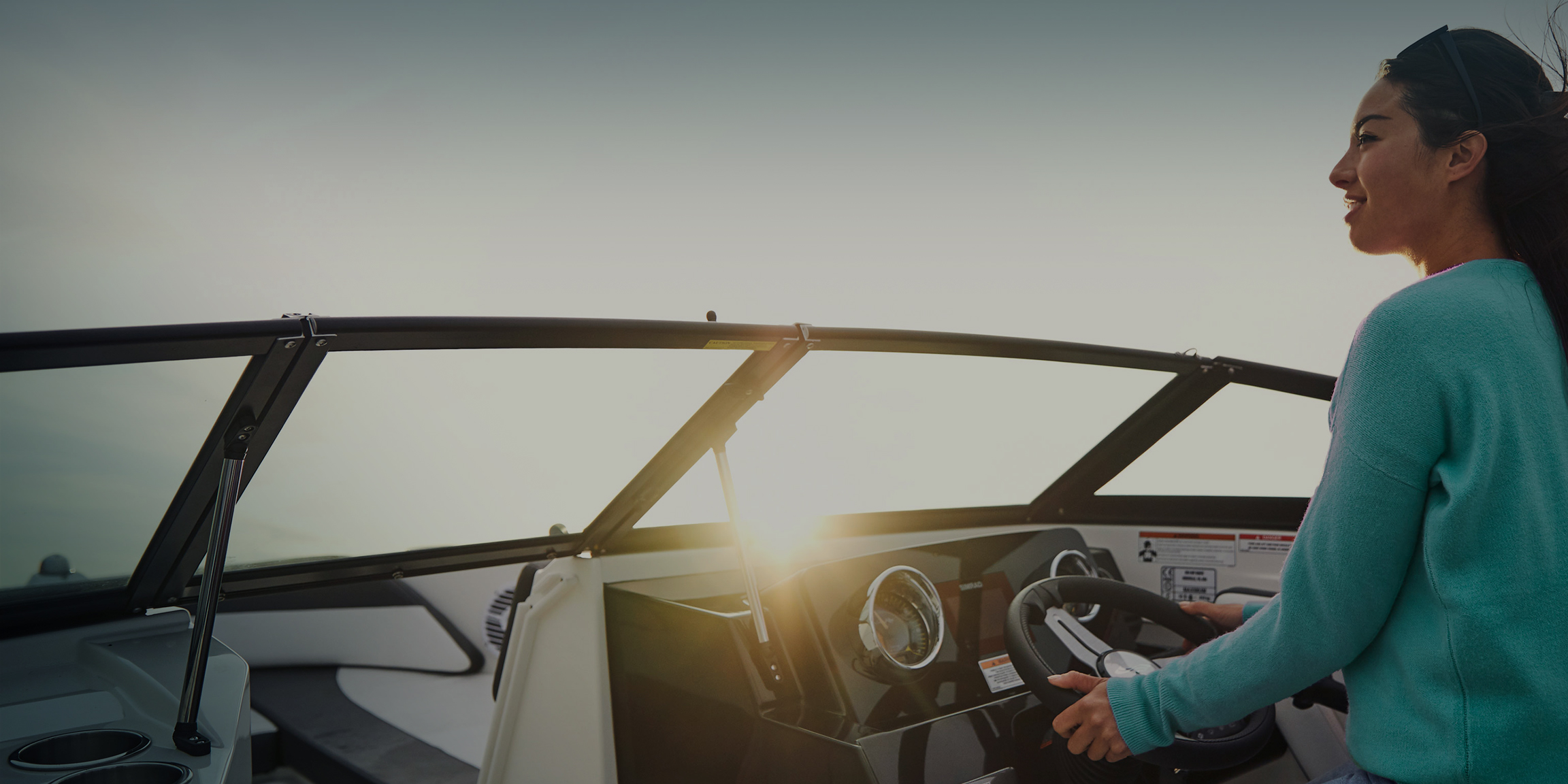 Woman in turquoise sweater driving a powerboat at sunset