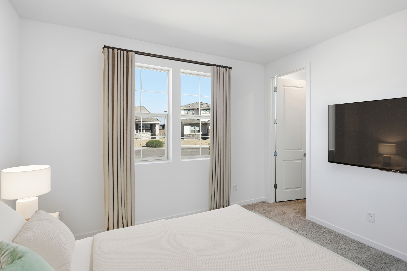 bedroom with a large white bed, a mounted tv, and a nightstand lamp