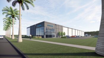 A square-shaped, one-story building is surrounded by grass and palm trees.