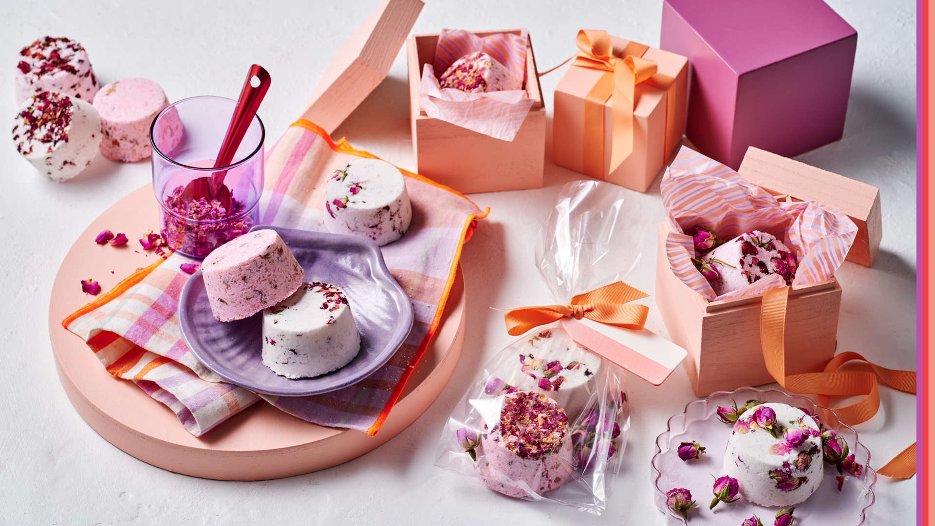 A selection of home made Rose infused bathbombs for Mother's Day, displayed in cello bag wrapped with apricot ribbon and gift tag. scattered gift boxes in hues of apricot, purples and pinks.