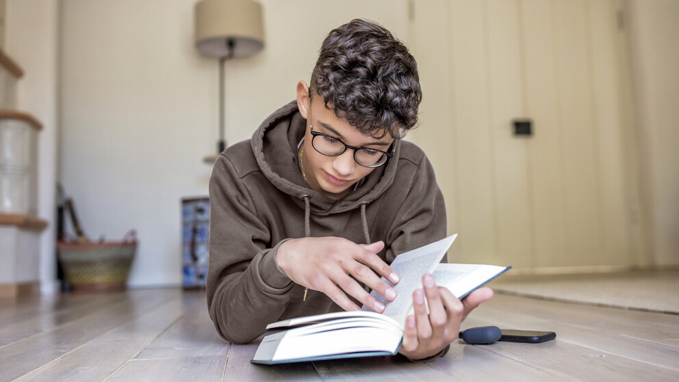 Boy with curly hair and glasses holding and reading a book