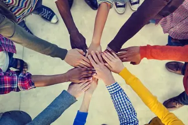 An overhead view of a group of people standing in a circle with their hands stacked on top of each other in the center, representing teamwork or collaboration.