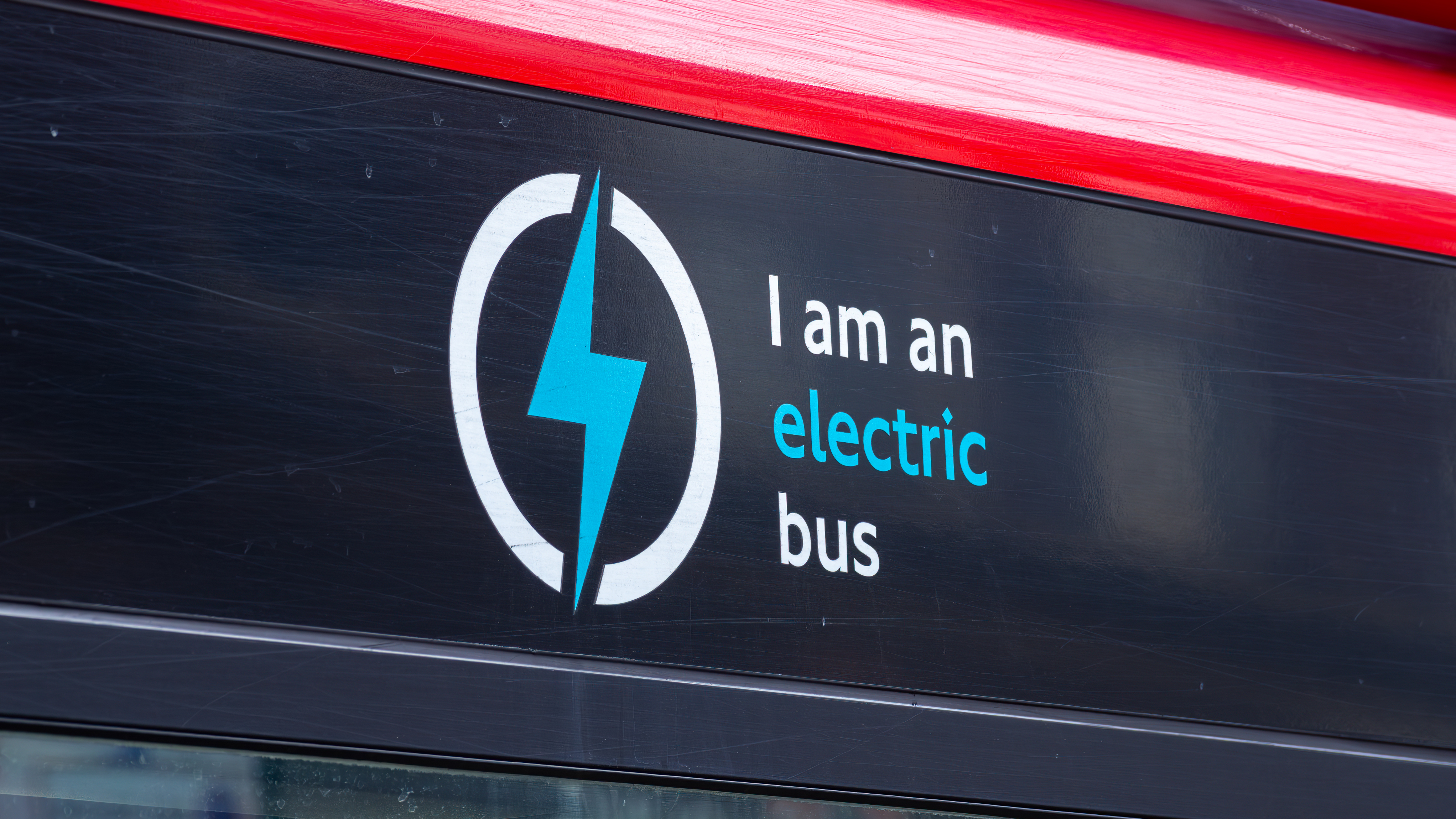 A close-up of a bus sign showing a blue lightning bolt icon with the words “I am an electric bus” printed beside it.
