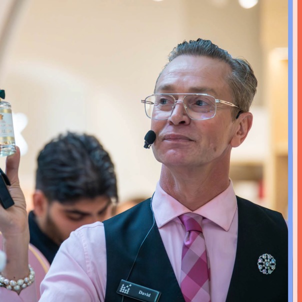 a man with glasses in a pink shirt holding a fancy bottle of fragrance 