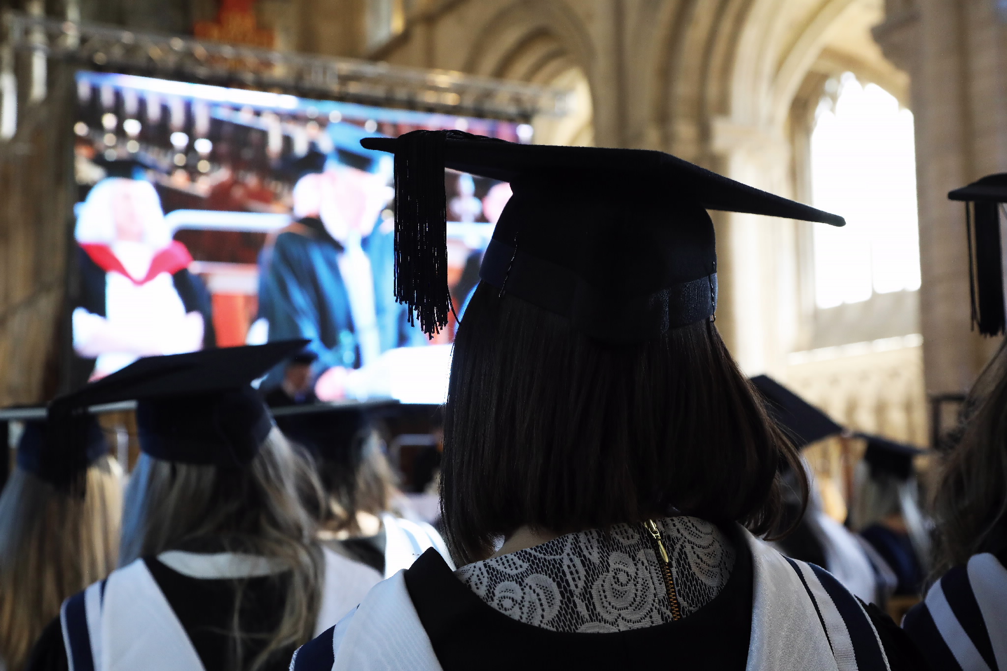 Graduates' caps and gowns facing a large screen during the ceremony