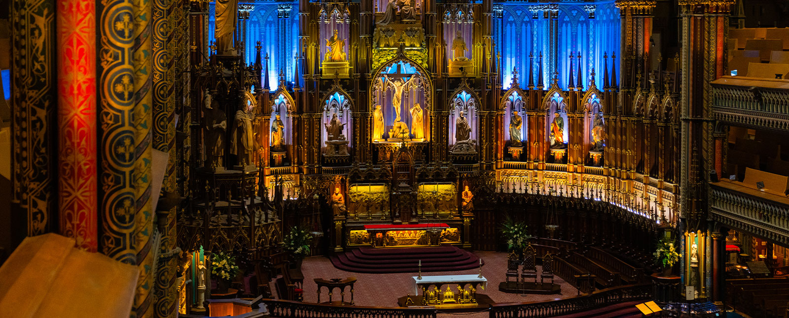 An elevated view of the ornate, beautifully lit altar and sanctuary inside the Montreal Notre-Dame Basilica, with detailed columns in the foreground.