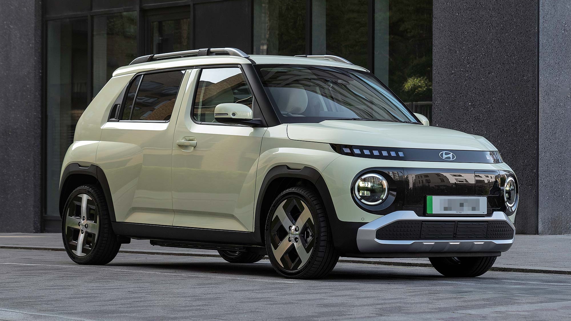 A pale green Hyundai Inster parked outside a modern building, shown from the front three quarter angle, available on the Motability Scheme.