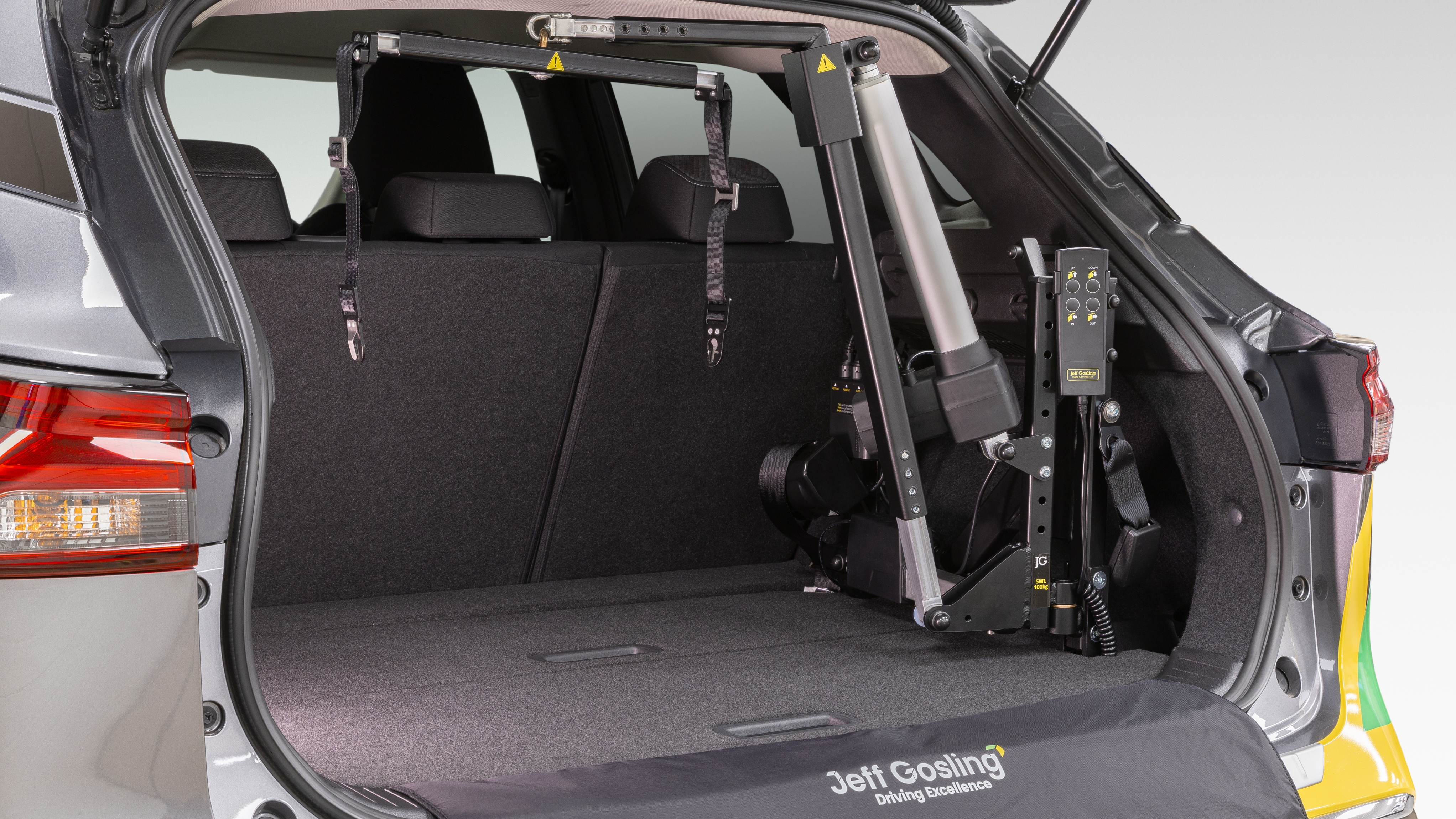 The boot of a grey SUV showing a Jeff Gosling electric hoist fitted inside. The hoist’s lifting arm and control box are neatly positioned beside folded rear seats, with branded protective matting along the boot floor.