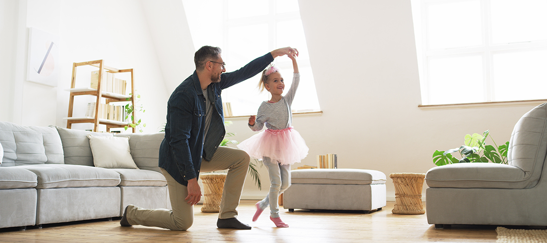 A white man dances with his young daughter in their home