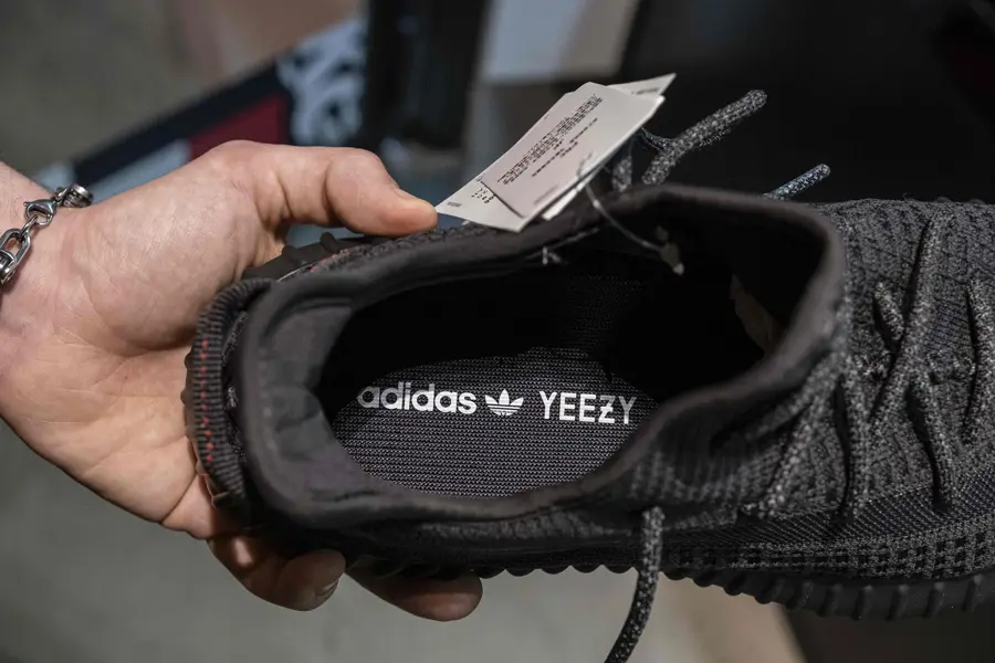 A hand holding a black adidas yeezy shoe with tags on