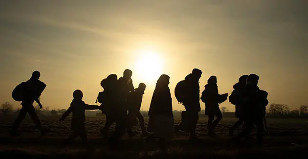 A sunset background wih silhouetted figures walking in a line, adults and children, most carrying baggage