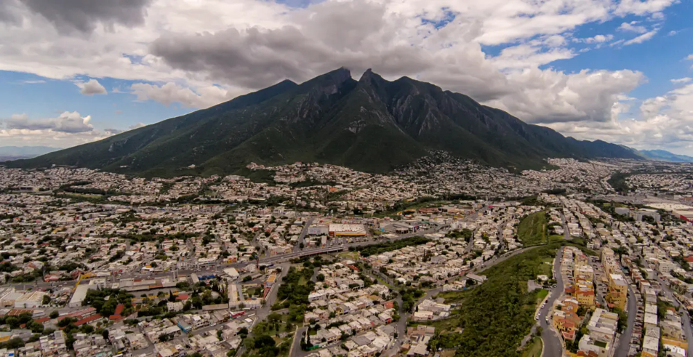 A photo of a mountain with the peak reaching the clouds and the foreground is houses and streets