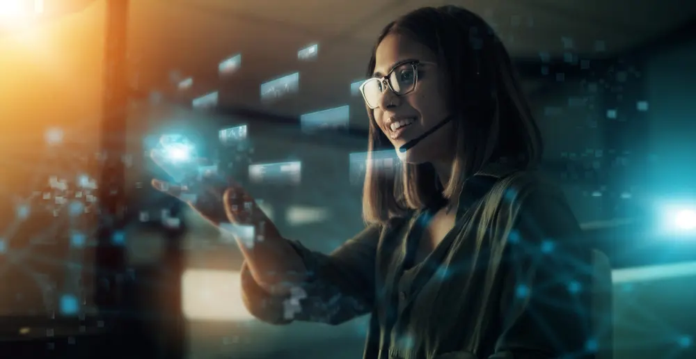 A woman wearing a headset and glasses with shoulder length straight hair smiling and touching a futuristic invisible touch screen
