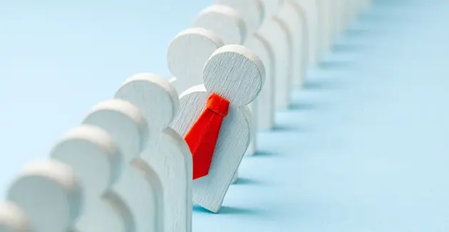 Wooden icons of people standing up in a row with one in the middle leaning out of the queue, wearing a red tie
