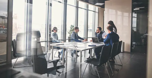 People in suits around a conference table in a conference room with big windows
