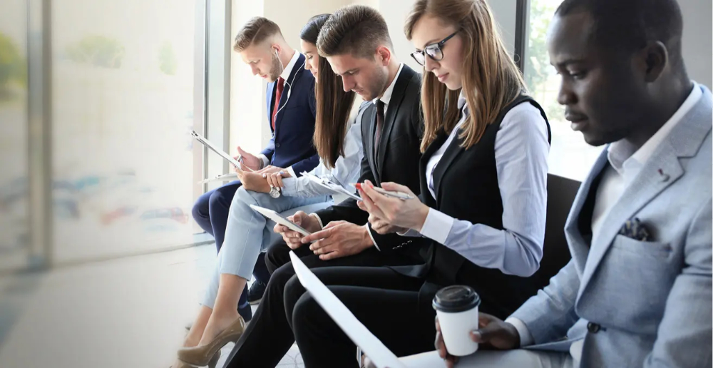 People wearing business attire sat in a row, each person is looking down at the clipboard they are holding, some have a pen