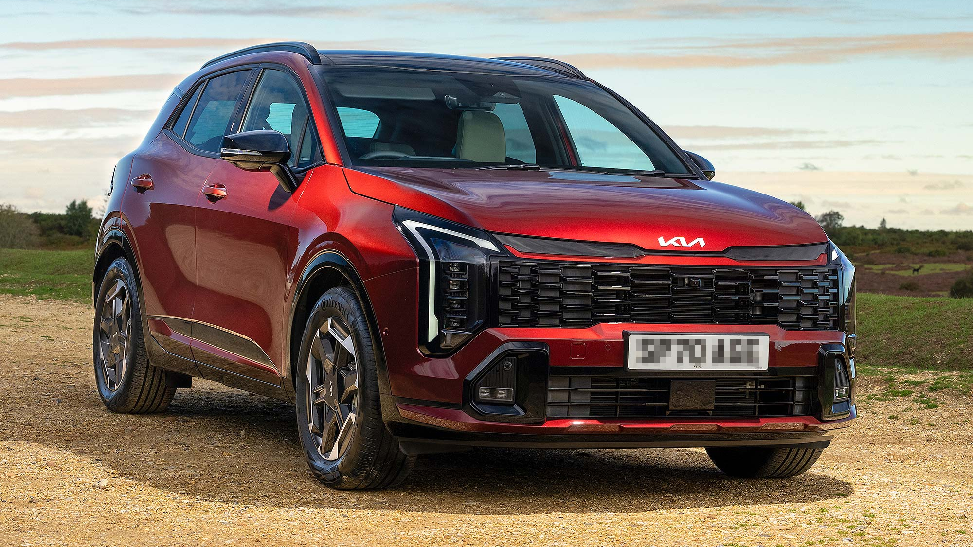 Red Kia Sportage SUV parked on gravel in open countryside, with a dramatic sky and landscape in the distance.