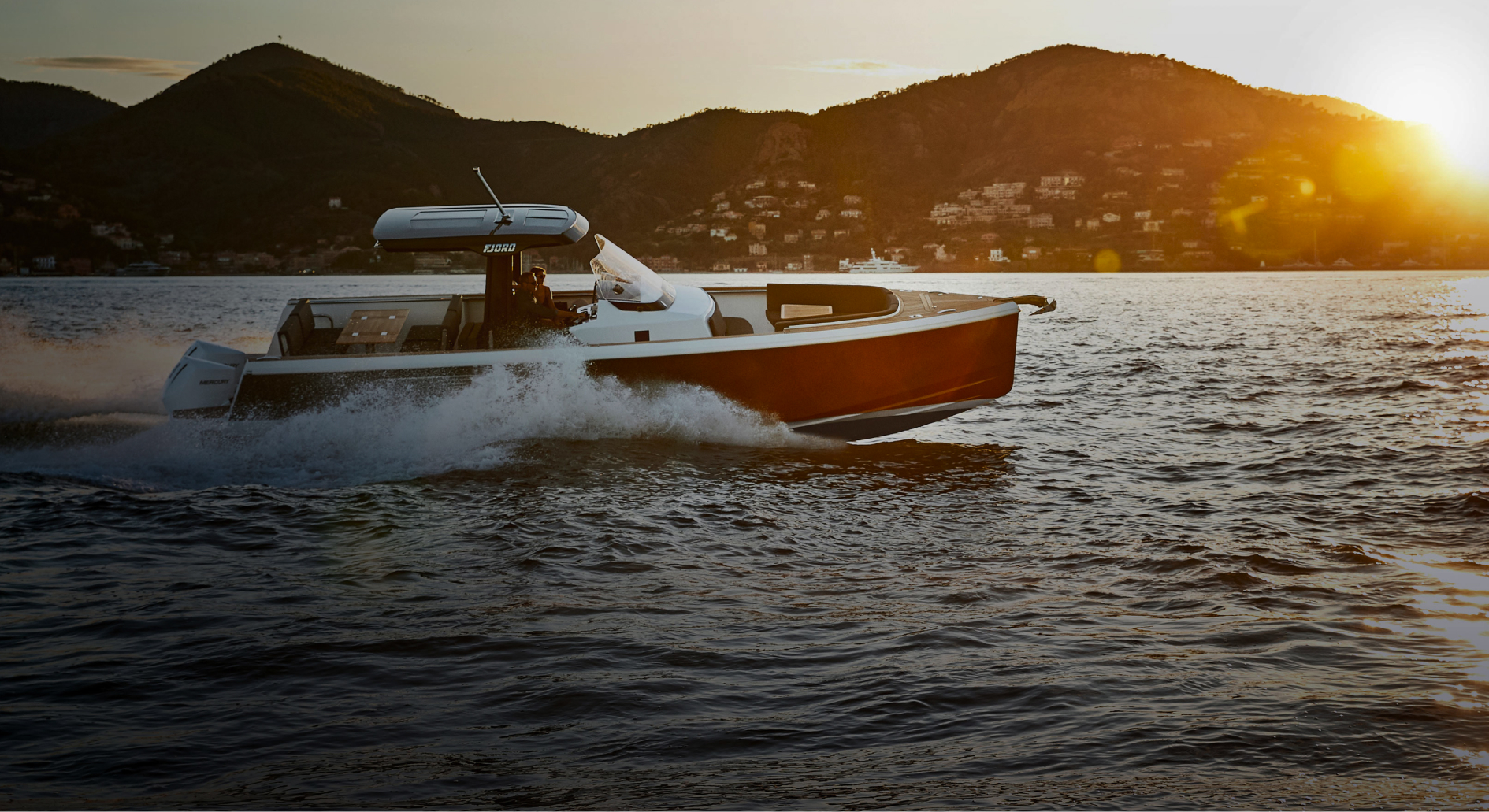 Red and white powerboat with onboard Fathom e-power system raching past distant coastal resort at sunset