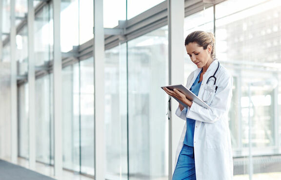 Doctor standing in a glass hallway looking at a tablet