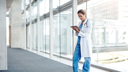 Doctor standing in a glass hallway looking at a tablet