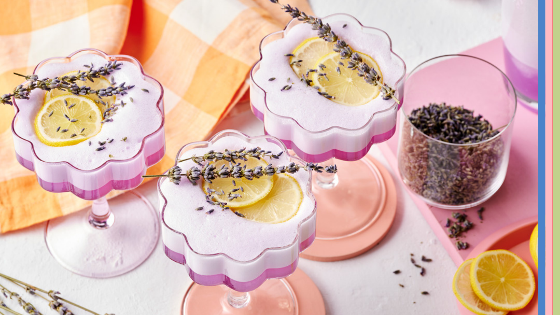 Three flower shaped cocktail glasses containing purple hued cocktail on white backdrop with cocktail shaker, lavender and lemon.