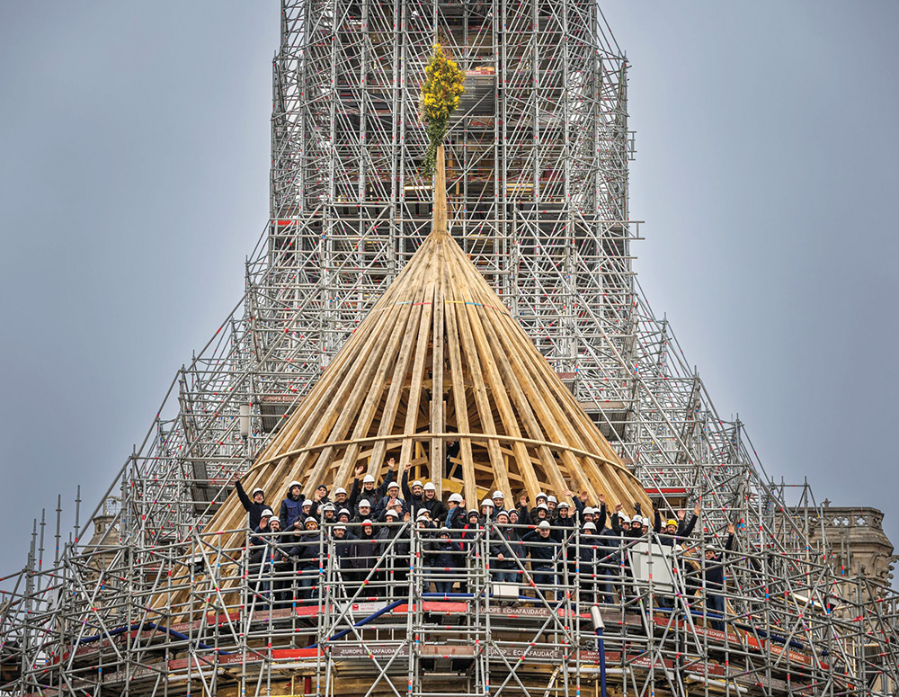 Jubilant craftsmen stand on the restored timber-framed roof of Notre Dame's choir.