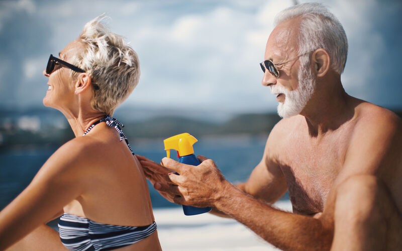 An older man puts sunblock on an older woman at the beach