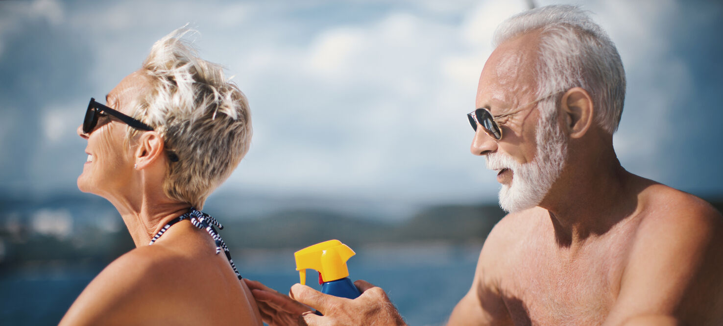 An older man puts sunblock on an older woman at the beach