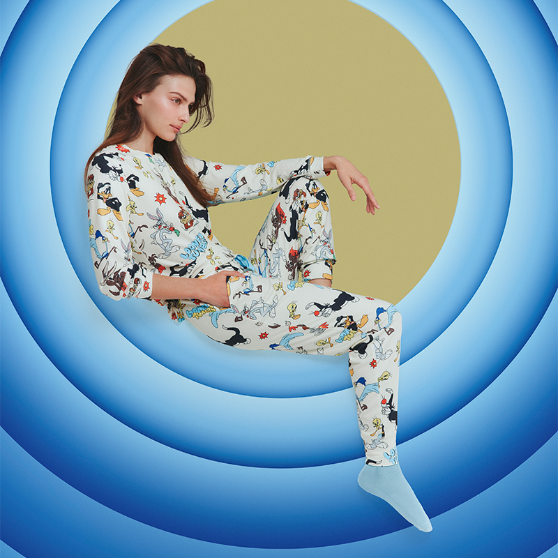 woman in cosy looney tunes themed pyjamas lies on the looney tunes background
