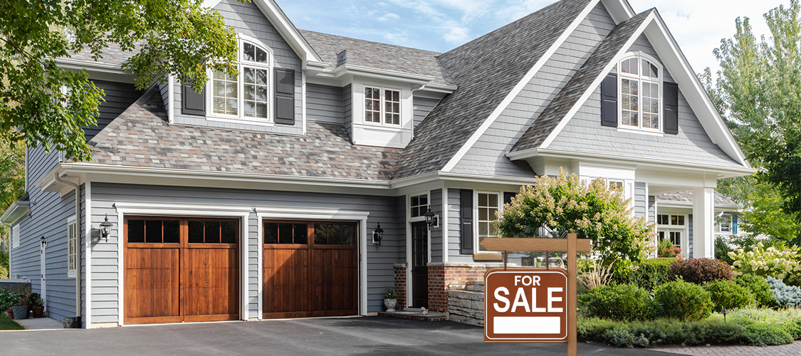 A grey, suburban house with a red 'For Sale' sign in the front yard.