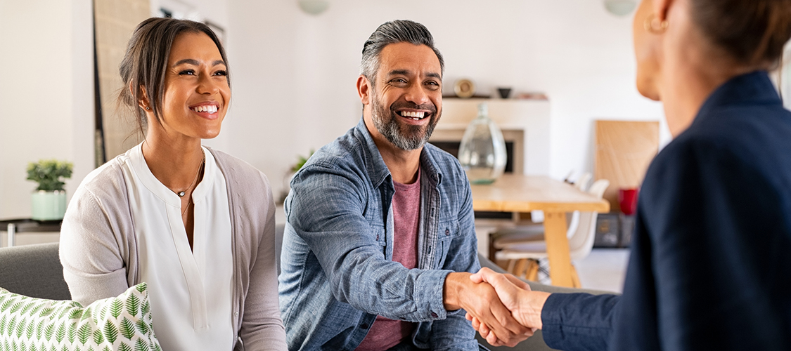 A couple sitting at a desk, shaking a woman's hand.