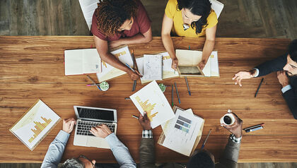 Overhead view of co-workers sitting at a wood table reviewing documents