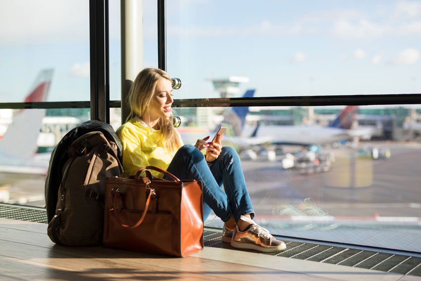 Mlado dekle se med čakanjem na potovanje z letalom zabava na telefonu.