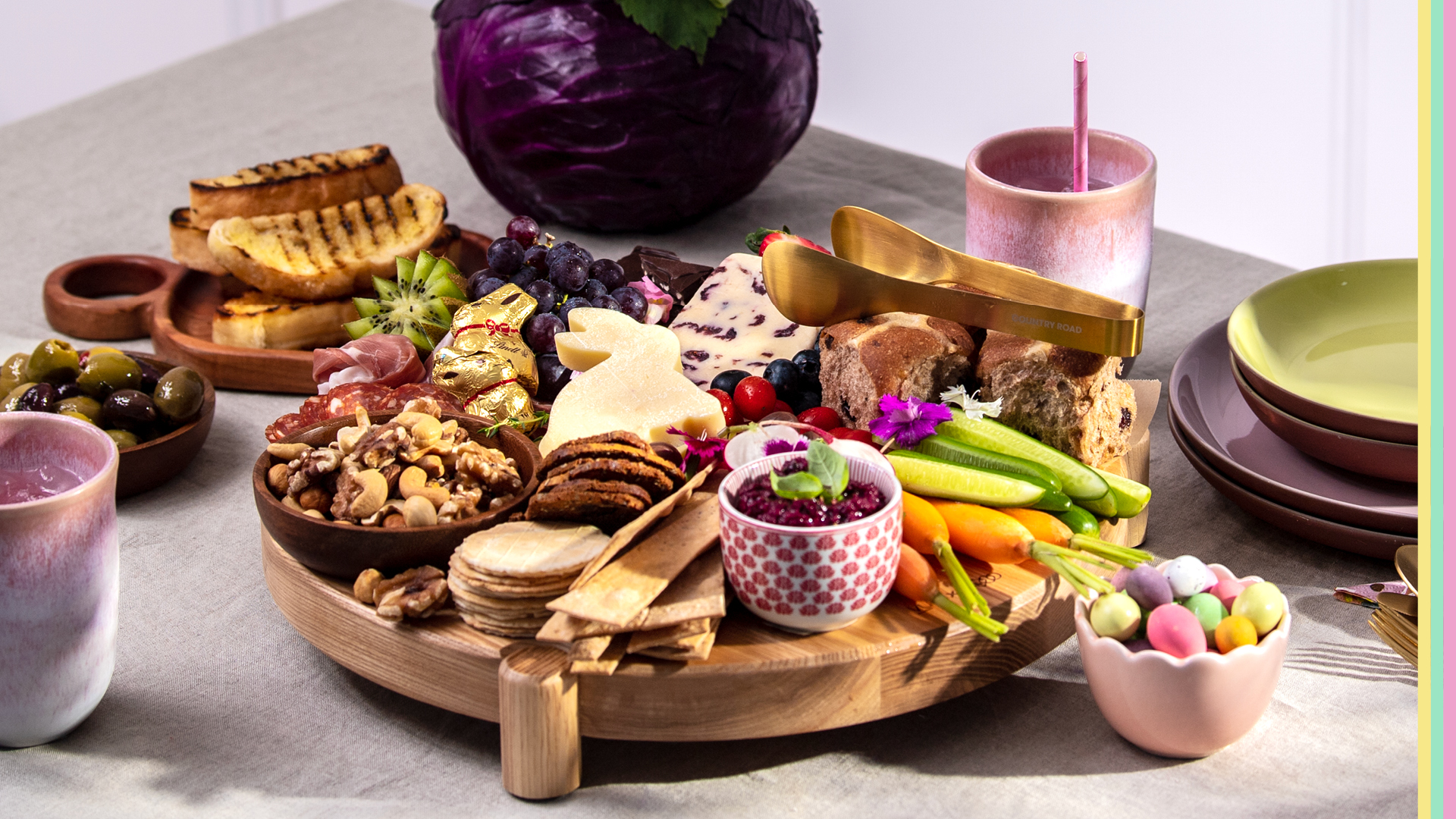 Easter inspired grazing platter featuring cheese, crackers, hot cross buns, carrots, cucumber, bread olives and more
