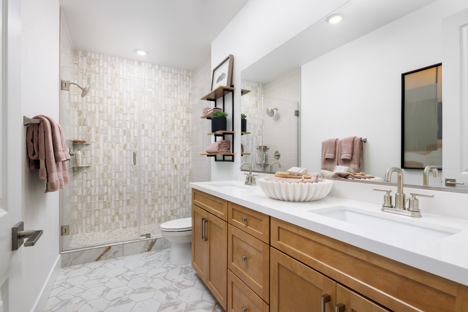 bathroom with light tan cabinets, white counters, two sinks, gray & white tile floors, and large walk-in shower with frameless glass enclosure