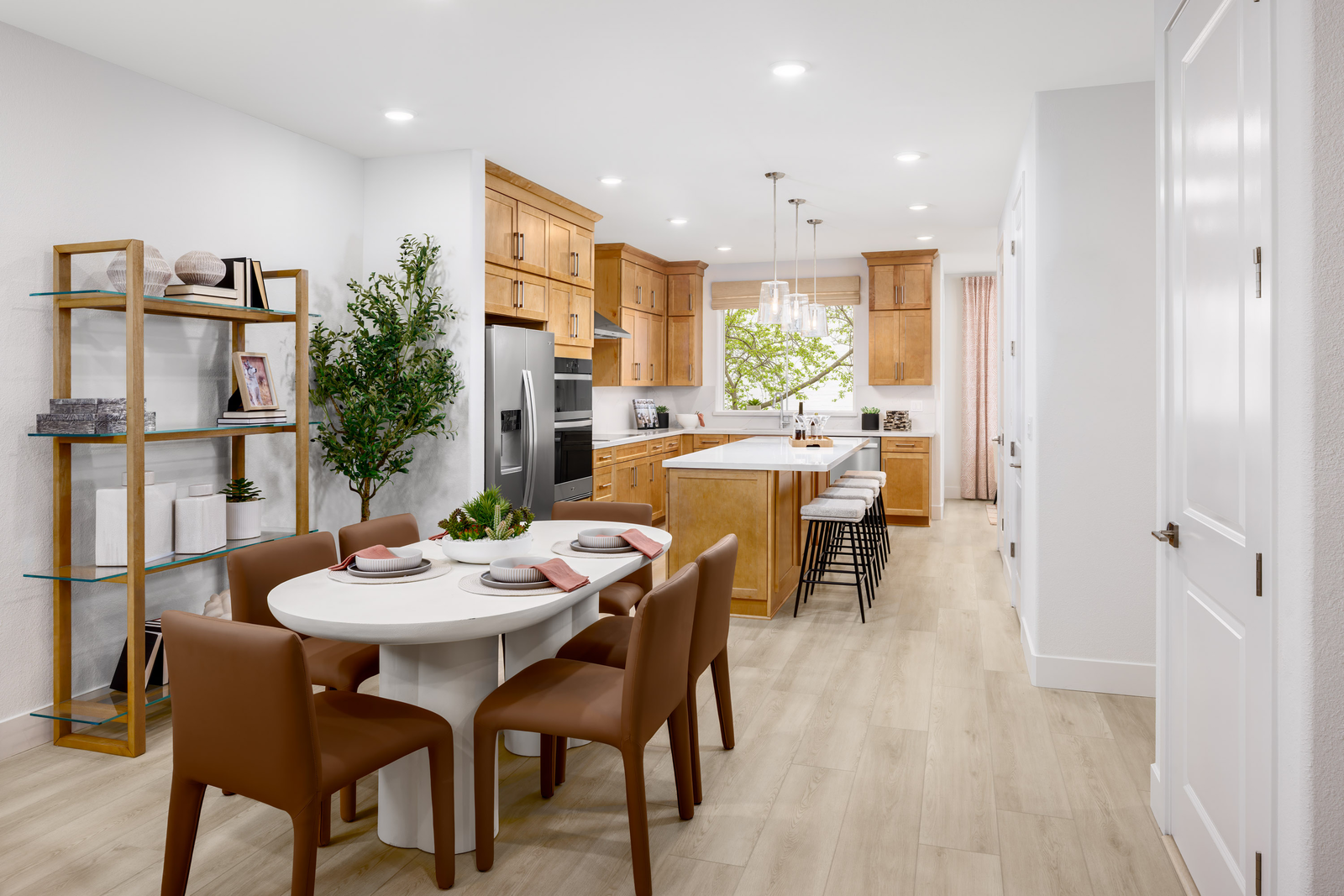 kitchen with white oval dining table & six brown chairs, light wood floors, and light brown wood stacked cabinets