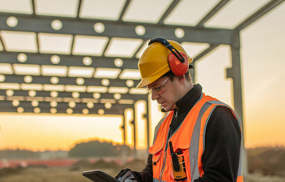 Construction worker at a work site at sunset, looking at a clipboard