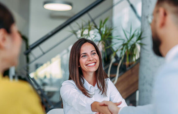 Woman shaking hands with a man across a desk while another coworker looks on