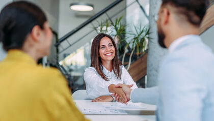 Woman shaking hands with a man across a desk while another coworker looks on