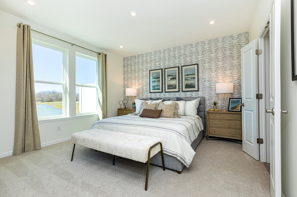 primary bedroom with wall paper and two windows 