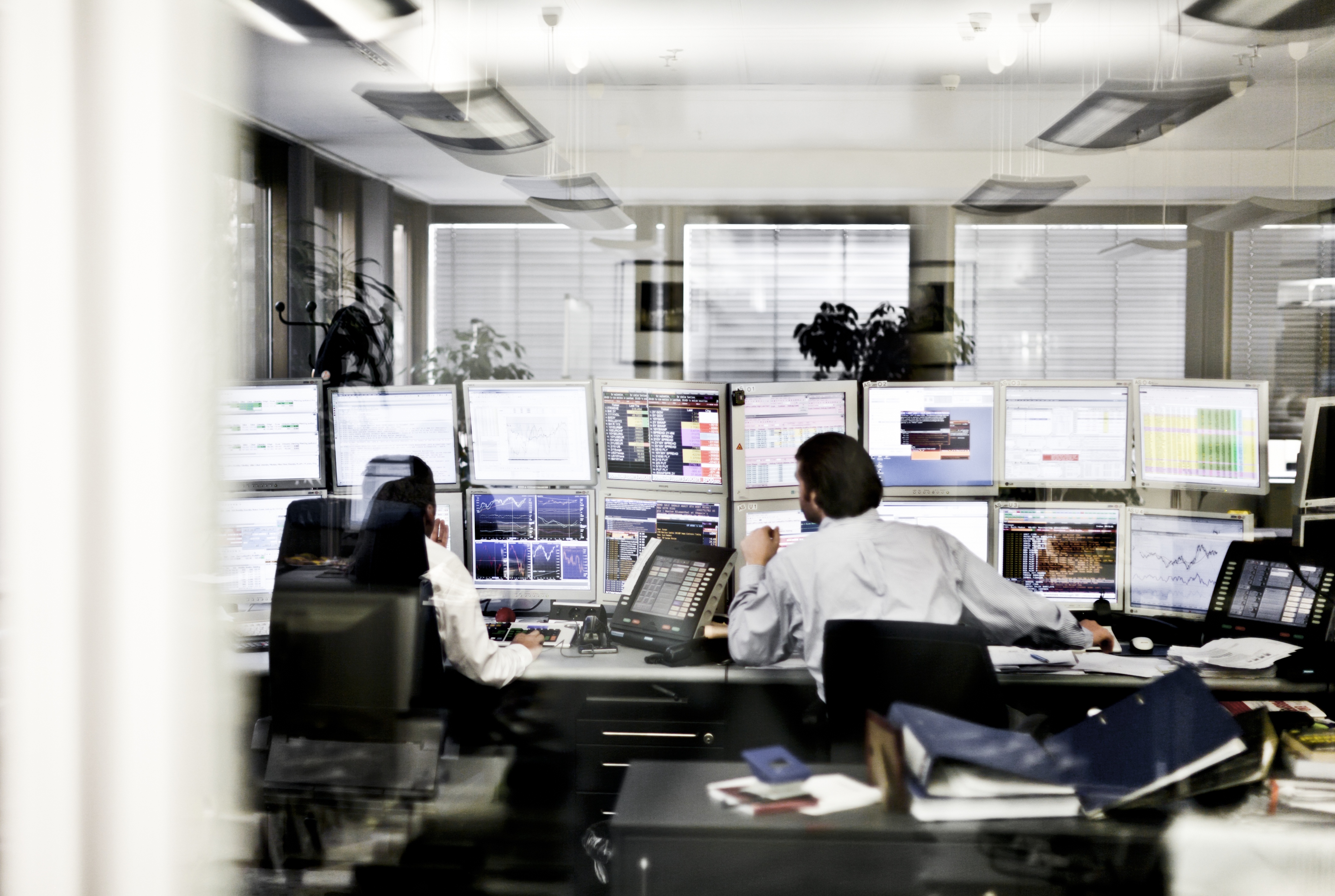 Image of two people sitting in fron of several computer screens.
